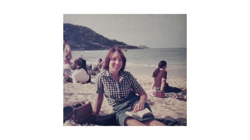 Woman sitting on a beach wearing blouse and skirt and smiling to camera