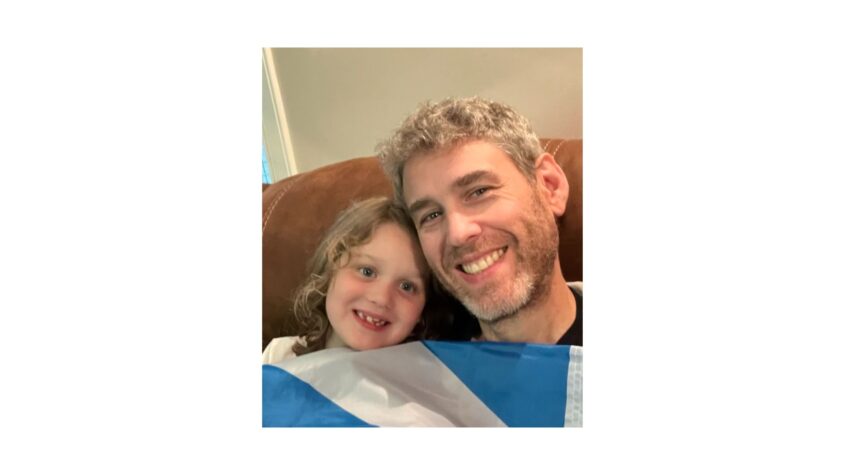 Young girl and father sitting down holding the soltaire flag over them