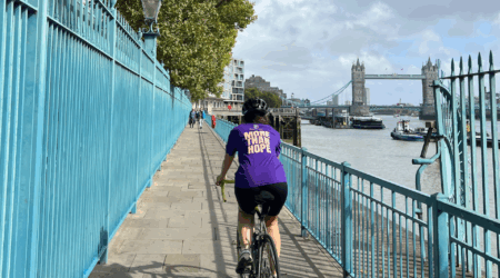women in a purple t-shirt reading 'More than Hope' riding a bike alongside the river thames