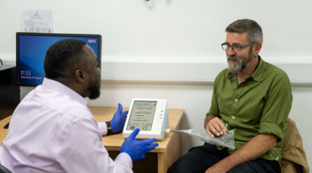 A man wearing gloves demonstrating a breath collection device to another man sat at a desk