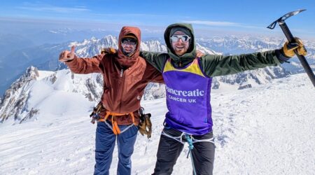 Two people on top of a mountain one wearing a pancreatic cancer vest