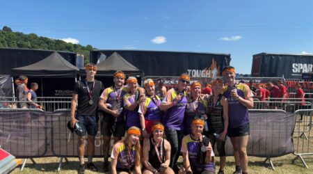 group of people wearing pancreatic cancer tops holding tough mudder medals