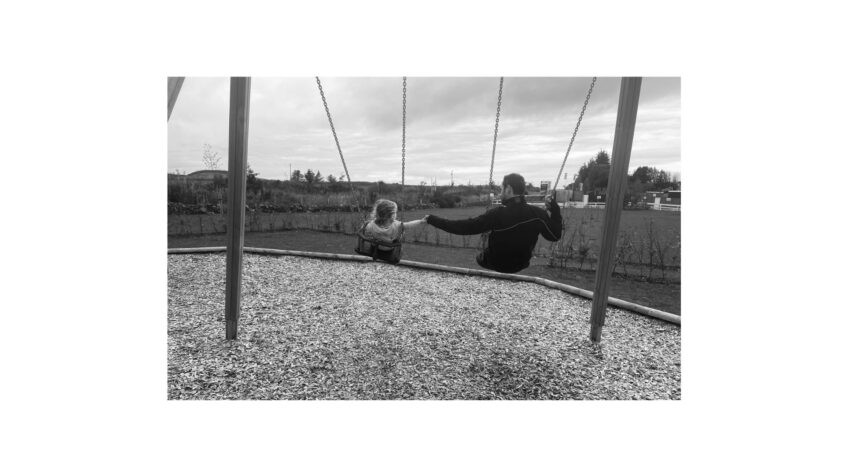 Black and white image of man and young girl on separate swings holding hands