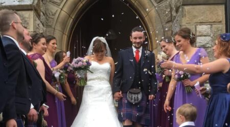 Bride in white dress and groom in kilt stepping out of the church