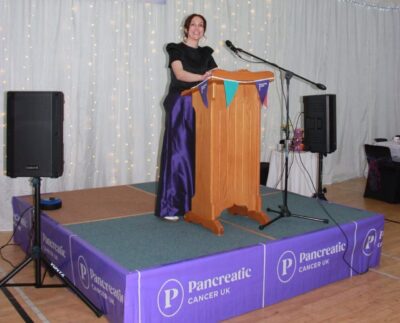 A women standing at a podium speaking  Purple Ladies Tea Party