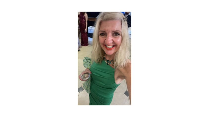 Middle age woman with blonde hair wearing smart green dress and smiling to camera