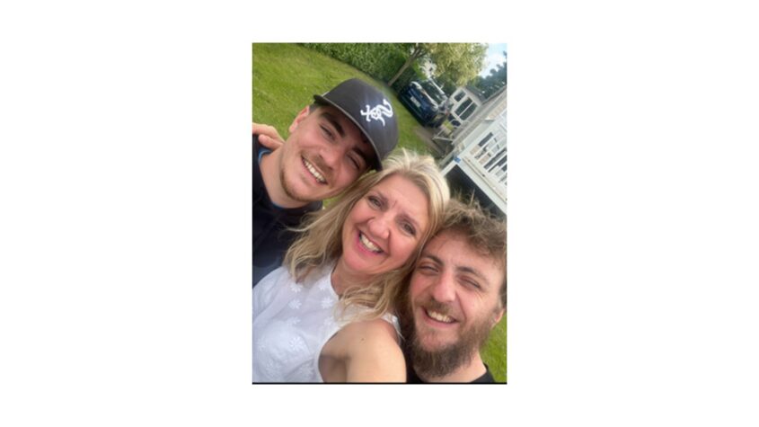 Middle age woman with blond hair in centre of selfie, with 2 younger men beside her, one on either side. All smiling to camera
