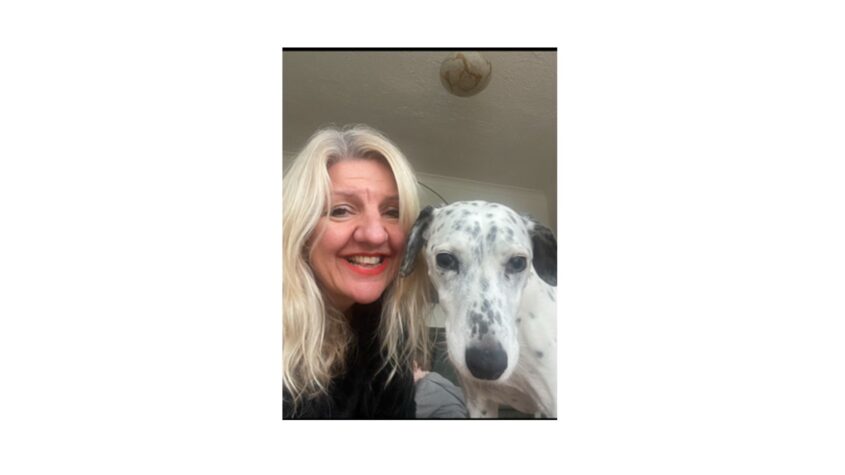 Middle aged lady with blonde hair with her white with black spots dog, both looking to camera