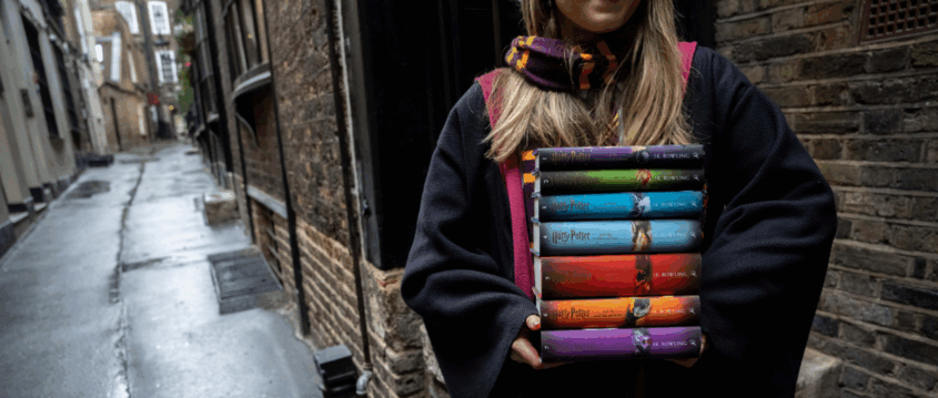 A person in a wizard robe holds a stack of colorful 