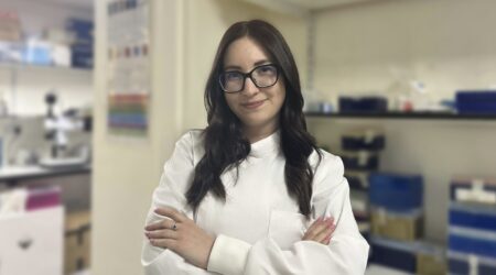 A young woman in a lab coat with her arms folded.