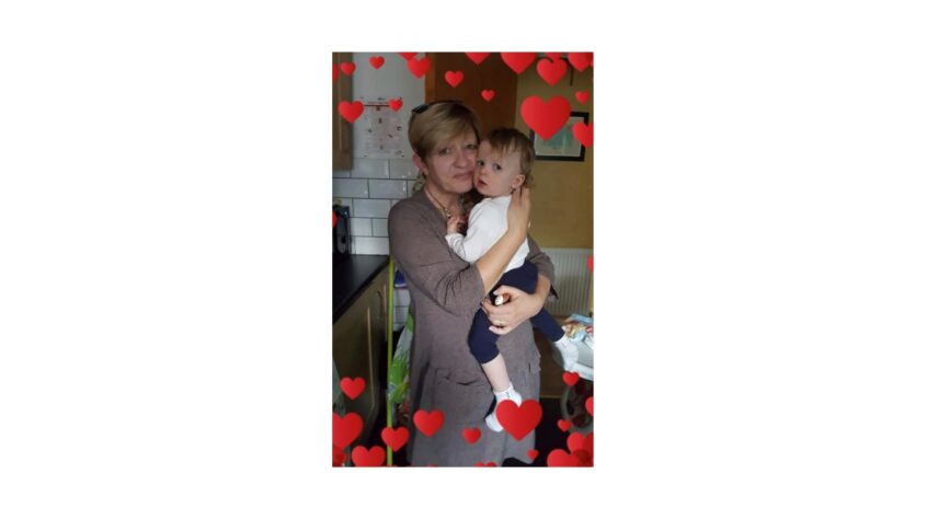 Middle aged lady holding an older baby in her arms, the image is surrounded by love hearts.