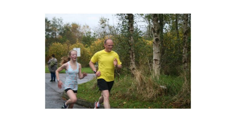 Man in yellow t-shirt running with his teenage daughter. they are on a road with trees behind them