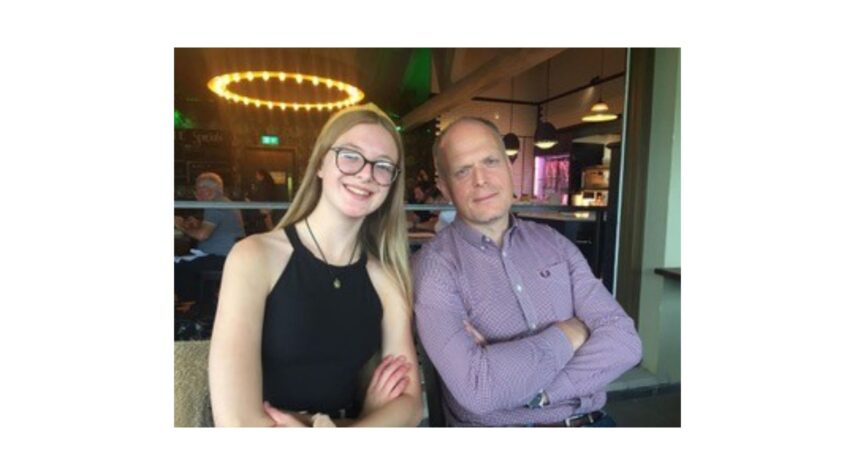 Father and daughter both with arms crossed, sitting in a restaurant, smiling with arms crossed