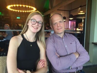 Father and daughter both with arms crossed, sitting in a restaurant, smiling with arms crossed
