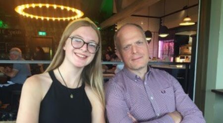 Father and daughter both with arms crossed, sitting in a restaurant, smiling with arms crossed