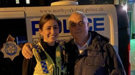 Younger woman in police uniform standing with her Dad in front of a police van