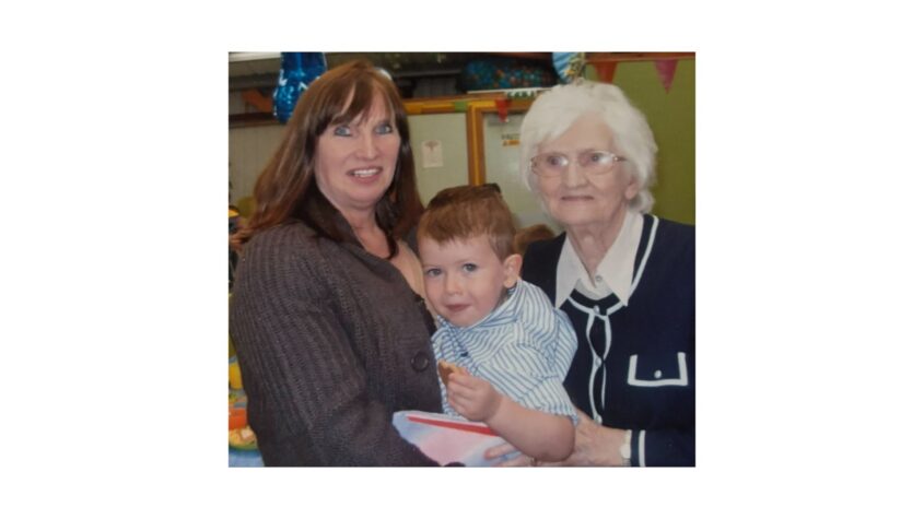 Elderly lady with her daughter, both holding a toddler and smiling to camera
