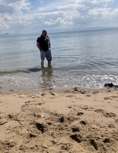 Man paddling in shallows of the sea, beach in foreground