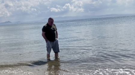 Man paddling in shallows of the sea, beach in foreground