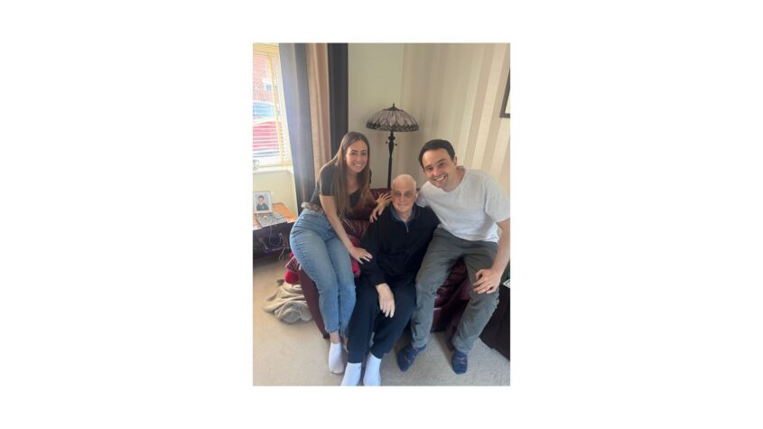 Older man sitting on armchair with younger man and younger woman sitting on either side