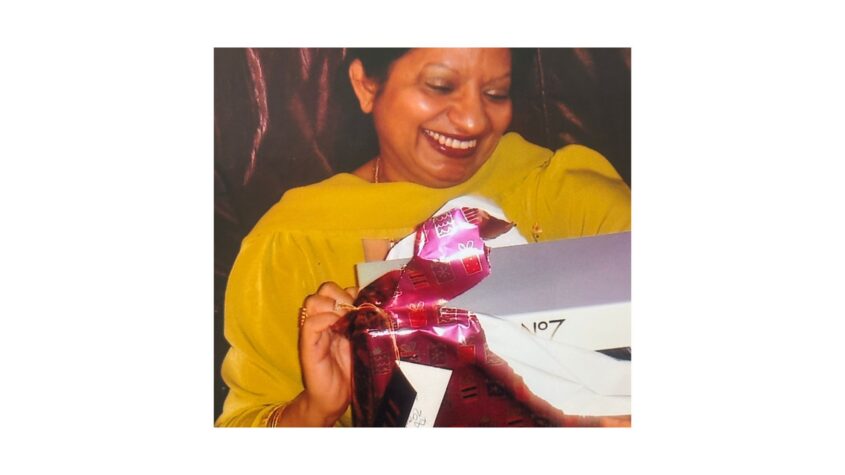 woman wearing yellow top and opening a gift, with a big smile