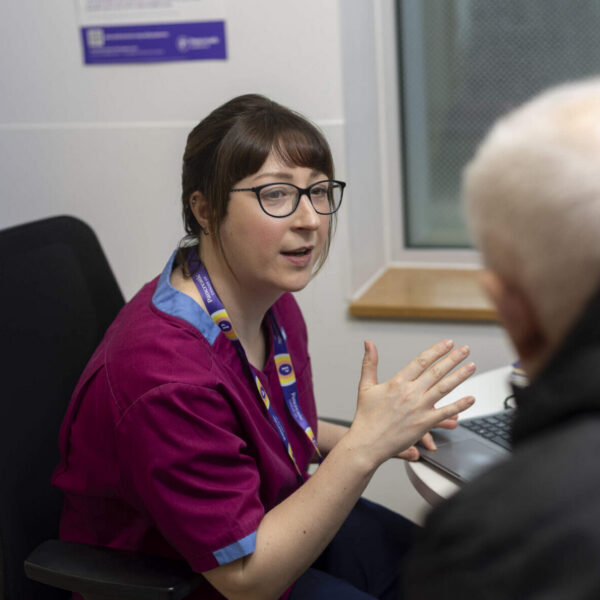 Older man with back to camera talking to health professional at her desk