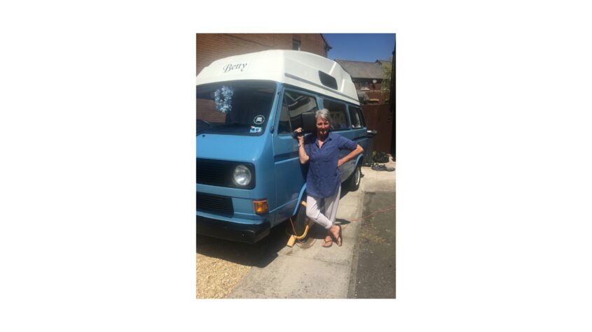 middle age woman standing in front of a blue camper van