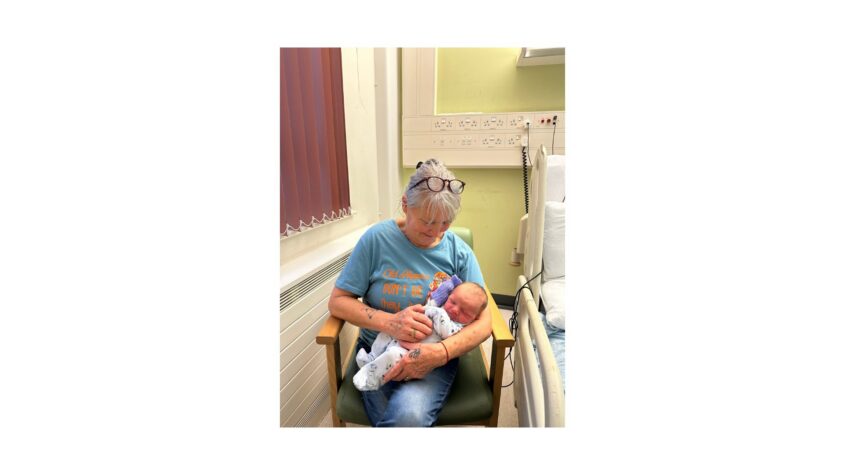 middle age woman sitting in a hospital chair, holding a newborn baby