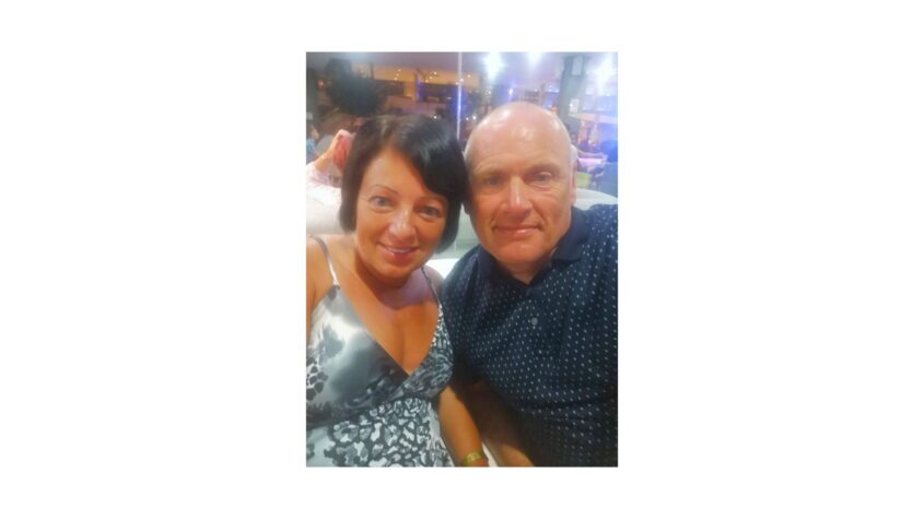 Man and woman sitting closely together, looking tanned and in summery clothes smiling to camera