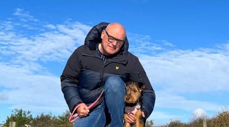 Man crouched down beside his dog, bright blue sky in background
