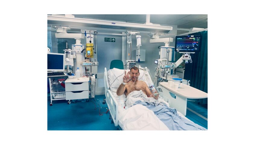 Man in intensive care bed, giving thumbs up to camera