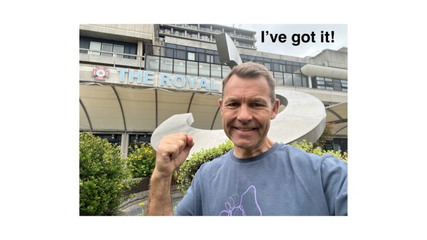 Man standing outside of hospital, smiling to camera with a pumped fist