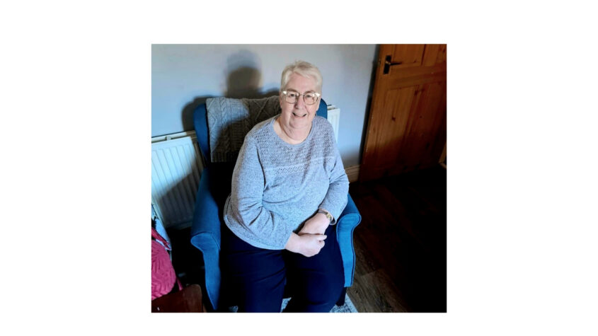 Older lady sitting in an armchair, smiling to camera