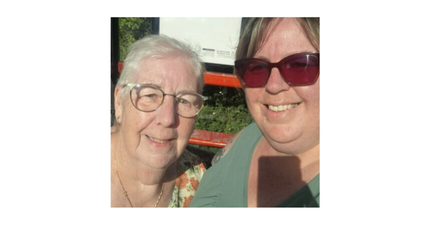 Older lady with her daughter, both smiling to camera with sunshine on their faces