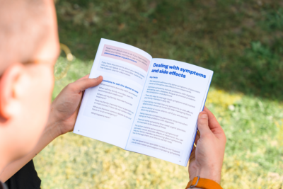 A person holds an open booklet outdoors, focusing on a section titled 