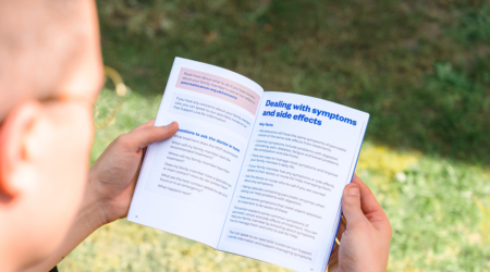 A person holds an open booklet outdoors, focusing on a section titled 