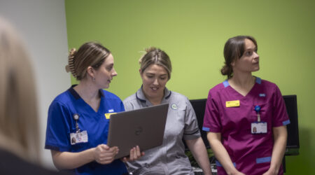 Three female health professionals gathered around a laptop in discussion